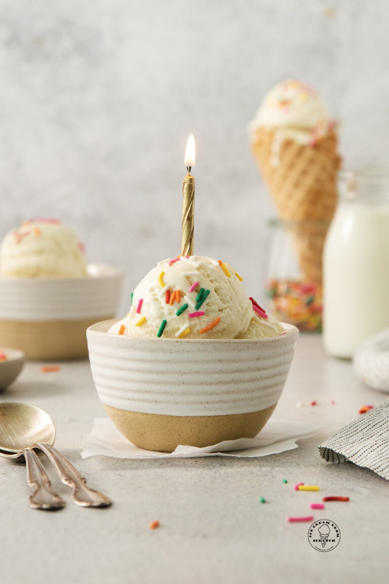 a ceramic bowl with scoops of ice cream, topped with sprinkles and a lit birthday candle.