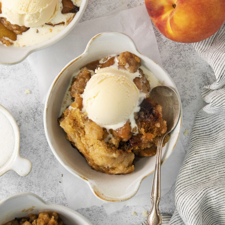 a ceramic crock filled with a serving of peach cobbler and vanilla ice cream