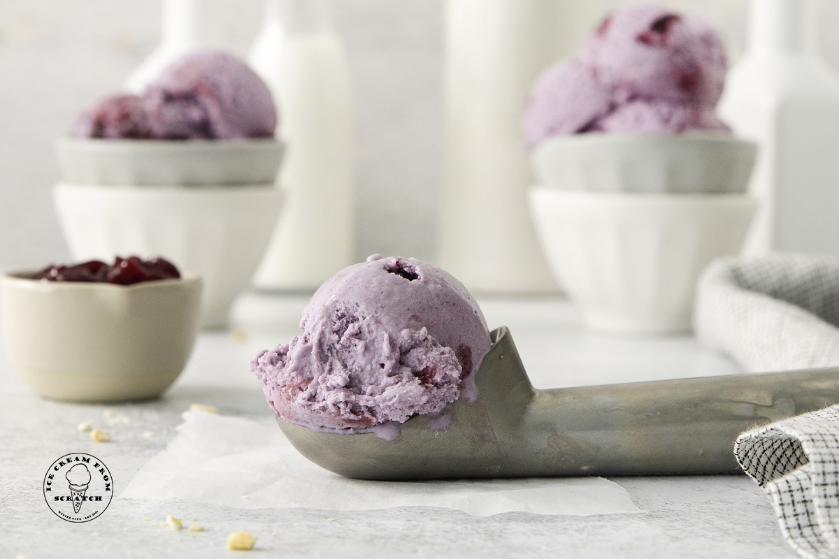 a metal ice cream scoop holding a scoop of grape flavored ice cream. 