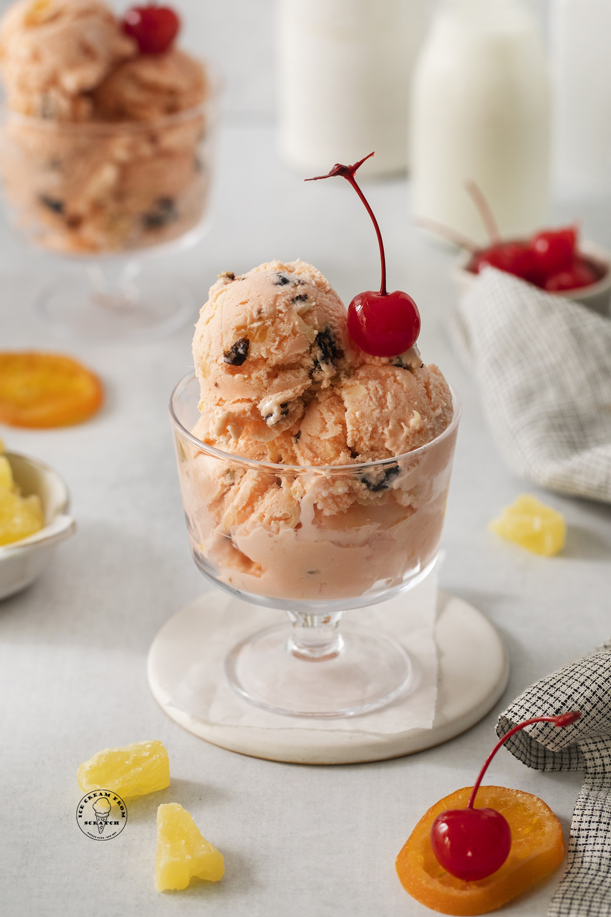 A footed glass dish of tutti frutti ice cream with a cherry on top.