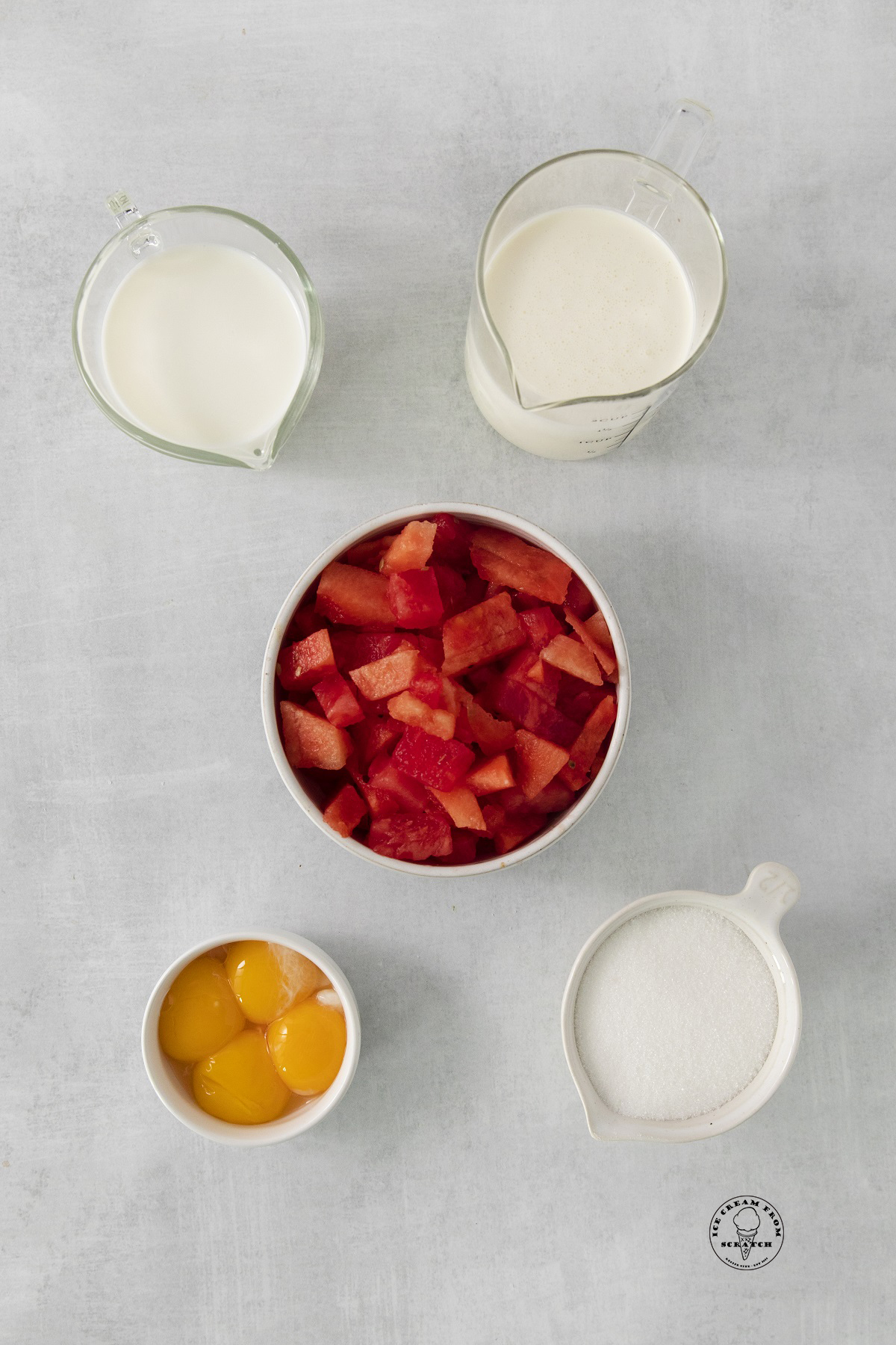A bowl of diced watermelon next to milk, cream, egg yolks, and sugar - the ingredients for making homemade watermelon ice cream.