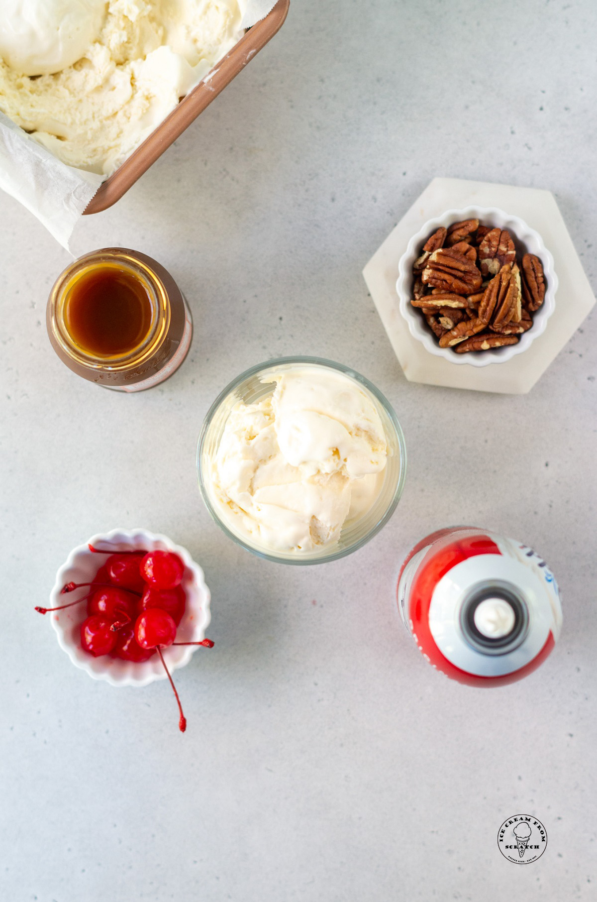 The ingredients in a turtle sundae, viewed from overhead, including pecans, caramel, and ice cream.