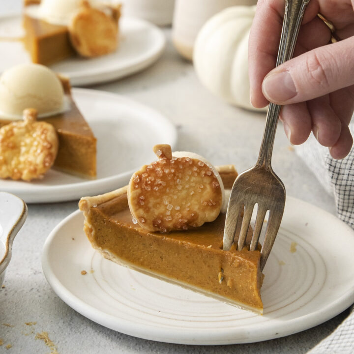 a slice of pumpkin pie with a pie crust pumpkin on top, eaten with a fork.
