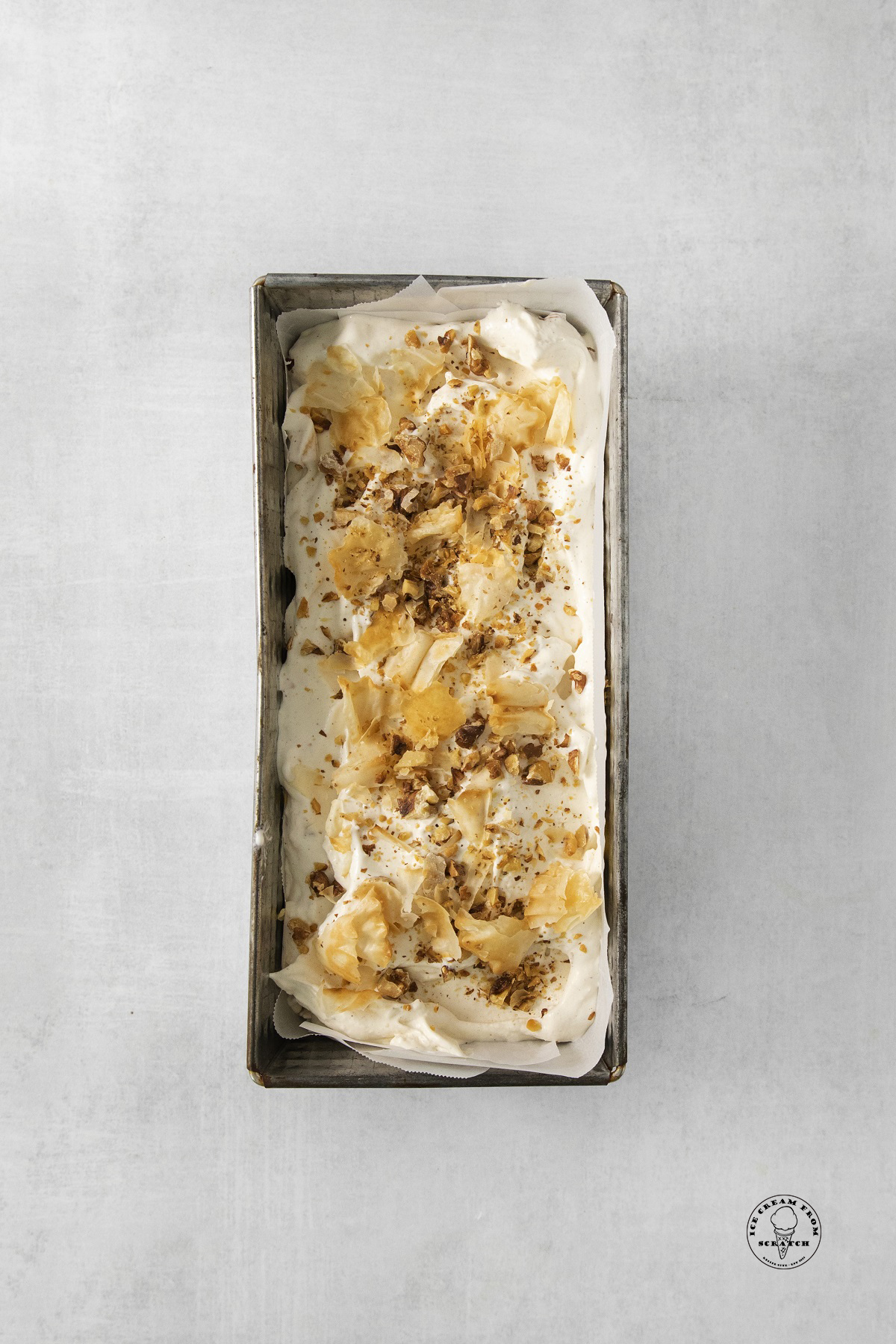 a metal bread tin filled with homemade ice cream topped with pastry shells and almonds like baklava.