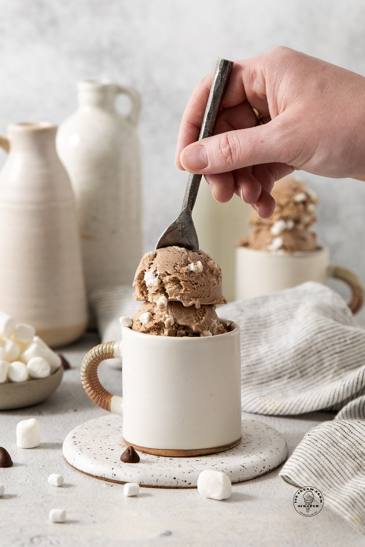 a hand holding a spoon, eating hot chocolate ice cream from a white ceramic mug.