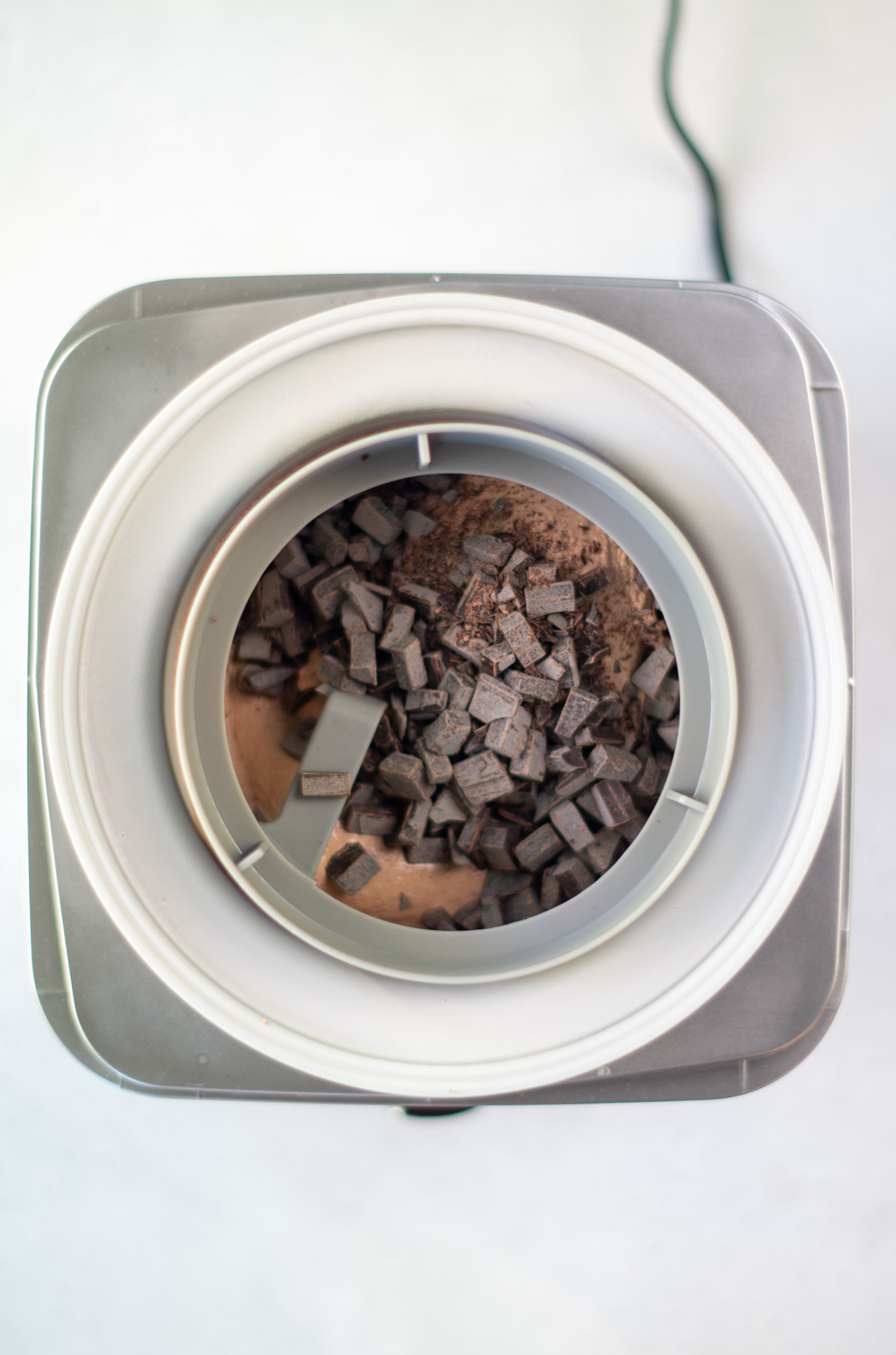 chocolate ice cream mixture in an ice cream maker bowl with chocolate chunks on top