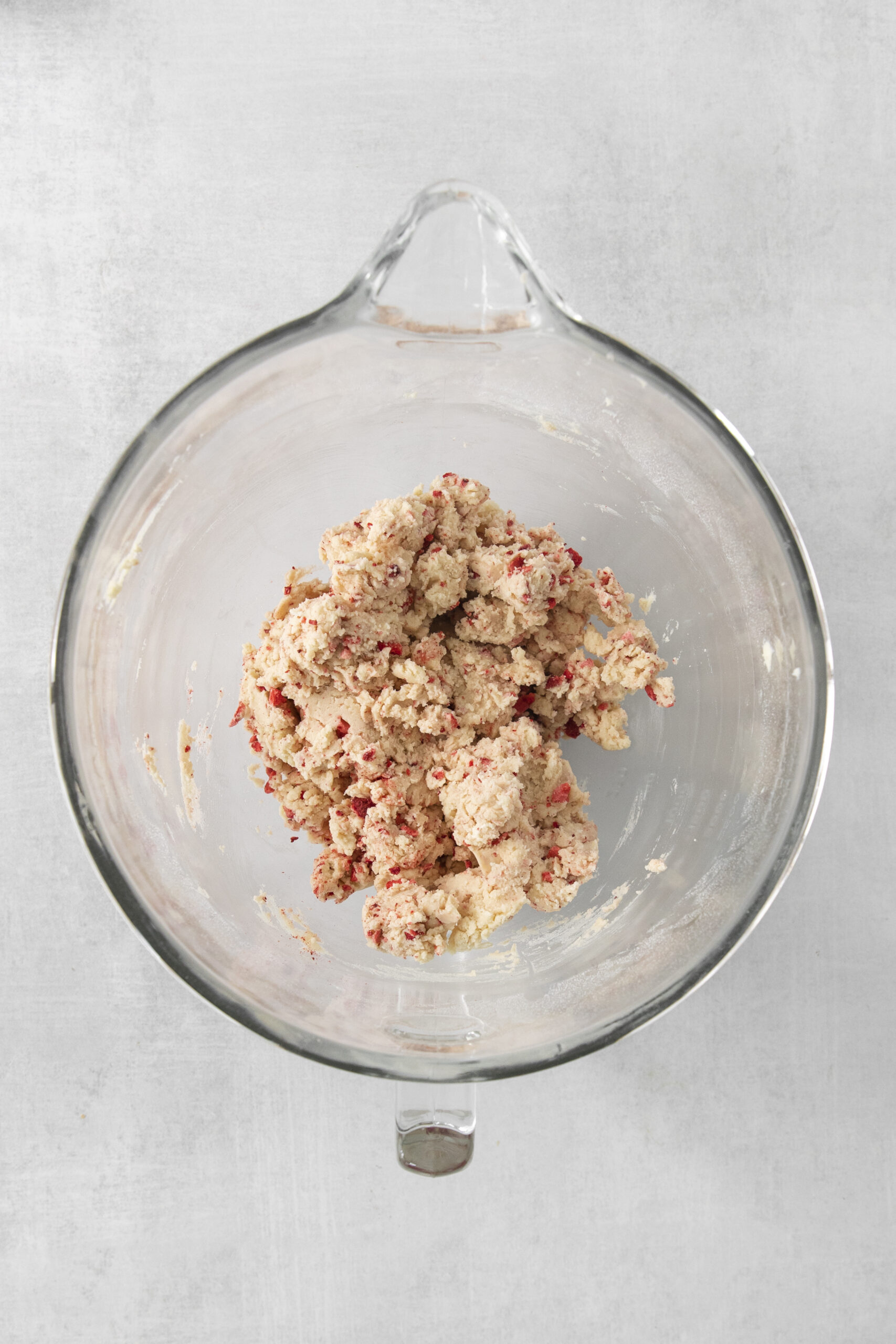 cookie dough in a clear mixing bowl with strawberries added